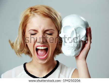 Young woman shouting and holding skull on gray background