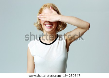 Portrait of a laughing woman closing her eyes with hand over gray background