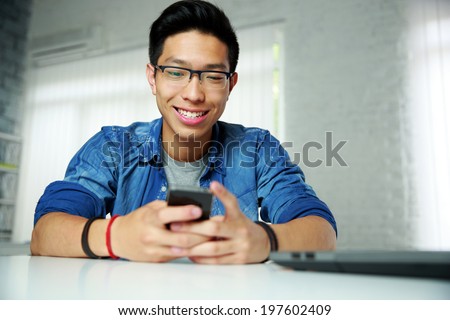 Portrait of a happy asian man sitting at the table with smartphone
