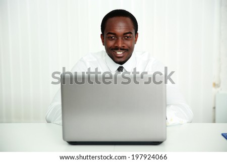 Portrait of a smiling african businessman sitting at the table with laptop in office