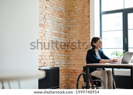 Young disabled business woman in wheelchair working at office desk and with laptop, accessibility and independence concept Foto stock © 