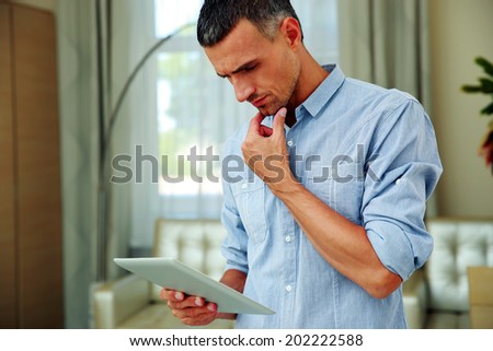 Handsome man standing and using tablet computer at home