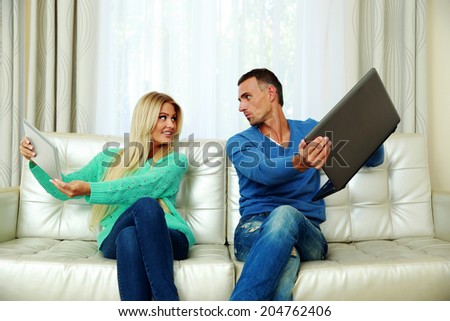 Funny couple sitting on the sofa with laptop and tablet computer at home