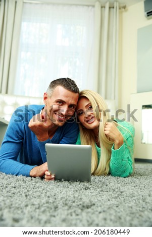 Happy couple lying on the carpet and using tablet computer together