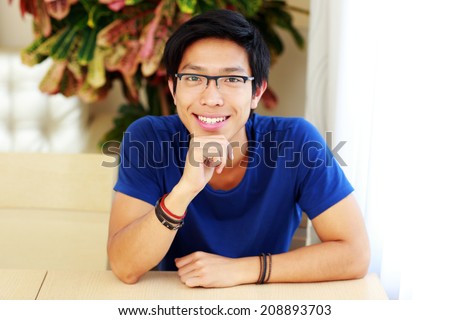 Smiling asian man wearing glasses sitting at the table