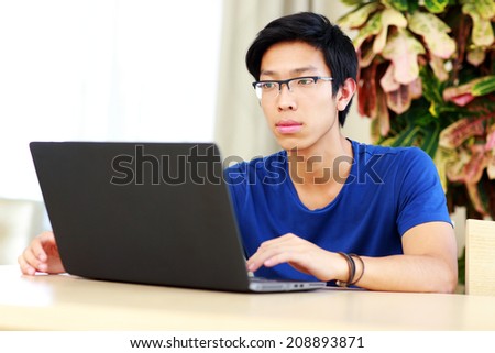 Serious asian man sitting at the table with laptop