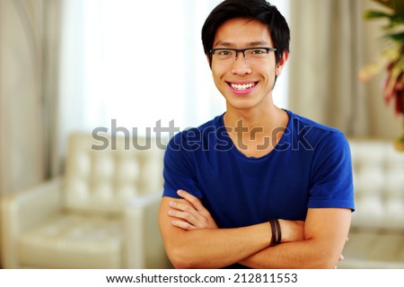Happy asian man standing with arms folded at home