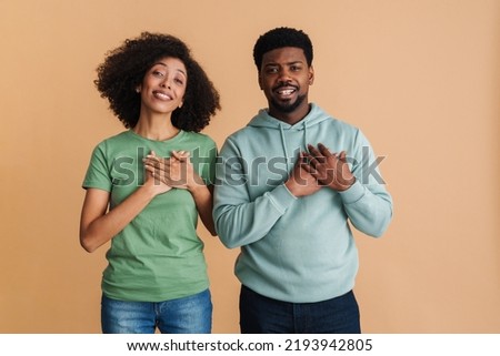 Black man and woman expressing dignity and keeping their hands at heart isolated over beige background Сток-фото © 