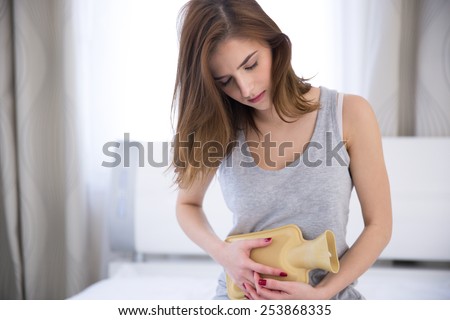 Young woman with hot water bottle on stomach on the bed