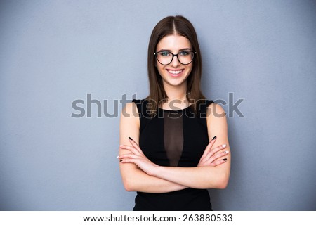 Portrait of a smiling woman in glasses and arms folded over gray background. Wearing in sexy black dress. Looking at the camera
