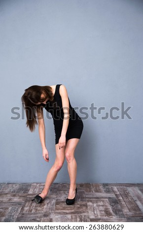 Full length portrait of a cute drunk woman in fashion black dress. Over gray wall. Sleeping while standing