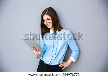 Happy businesswoman using tablet computer over gray background. Wearing in blue shirt and glasses