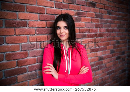 Portrait of a happy woman with arms folded standing over brick wall. Looking at camera. Wearing in red sportive jacket