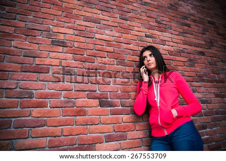 Young woman talking on the phone over brick wall and looking away