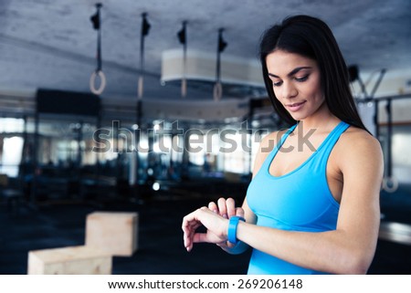 Happy young woman using activity tracker in fitness gym