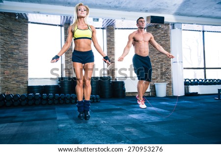 Handsome muscular man and beautiful sporty woman workout with jumping rope in crossfit gym