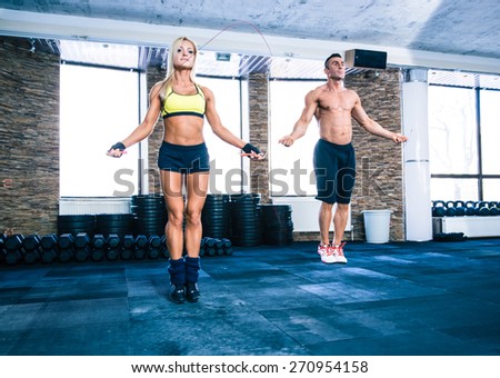 Muscular man and beautiful sporty woman workout with jumping rope in crossfit gym