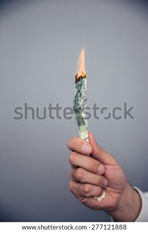 Male hand holding a burning US dollar bill over gray background