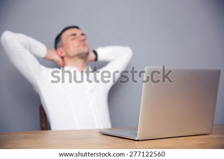 Tired businessman sitting at the table with laptop in office. Focus on laptop