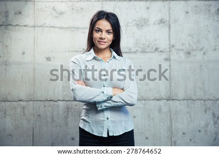 Portrait of a smiling businesswoman standing with arms folded over concrete wall and looking at camera
