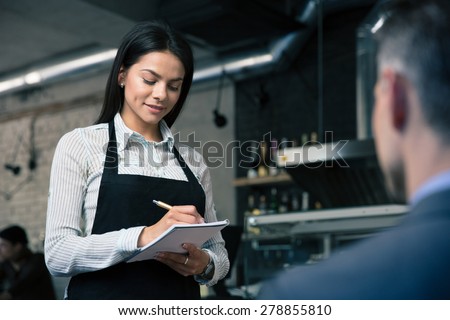 Female waiter in apron writing order in restaurant