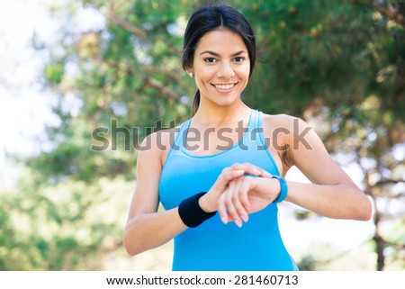 Smiling sporty woman using smart watch outdoors and looking at camera