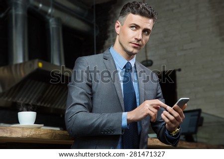 Handsome businessman holding smartphone and looking aside in cafe