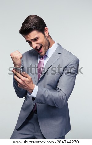 Happy businessman holding smartphone and celebrating his success over gray background