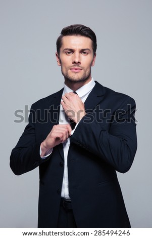 Confident businessman straightening his tie over gray background and looking at camera