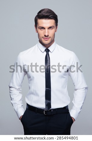 Young businessman standing with hands in pocket over gray background