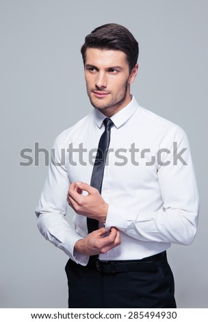Handsome businessman buttoning shirt over gray background