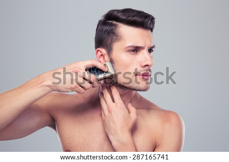 Handsome man shaving with electric razor over gray background