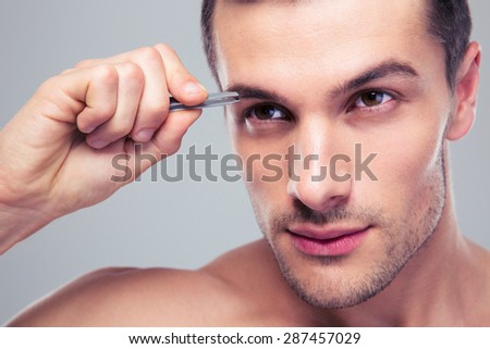Man removing eyebrow hairs with tweezing over gray background