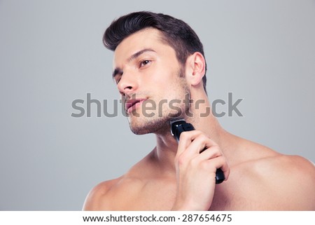 Young handsome man shaving with electric razor over gray background