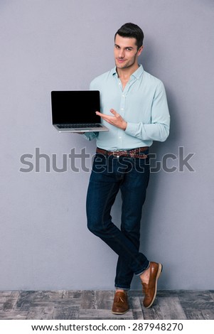 Full length portrait of a casual man showing blank laptop screen over gray background