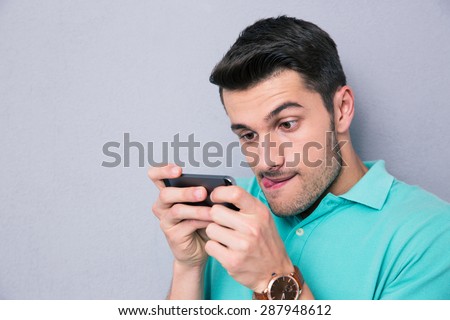 Funny young man using smartphone over gray backgrpound