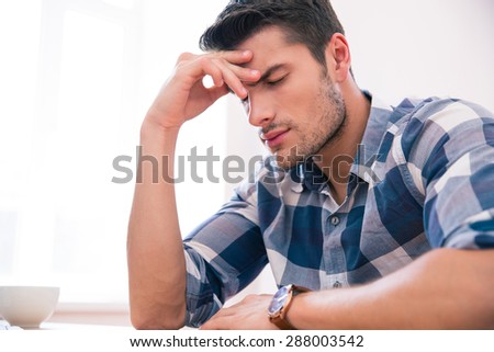 Casual businessman sitting at the table with headache in office