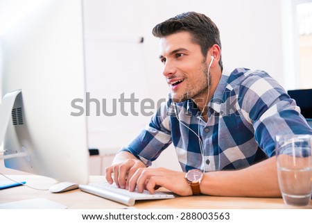 Happy young businessman in headphones using PC in office