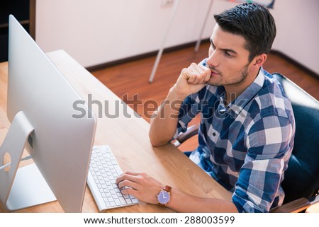 Handsome businessman in casual cloth sitting at the table and using personal computer in office