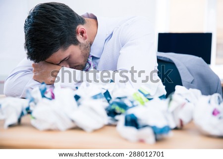 Tired businessman sitting at the table with crumpled of paper in office