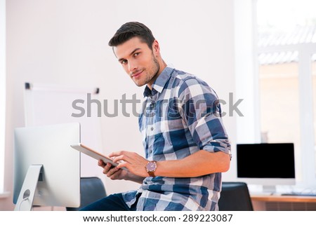 Businessman in casual cloth using tablet computer and looking at camera in office