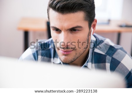 Portrait of a handsome young businessman with headphones using PC in office