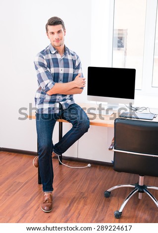 Full length portrait of a smiling businessman sitting on the table in office and looking at camera