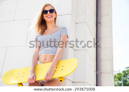 Portrait of a cute female teenager in sunglasses standing with skateboard outdoors