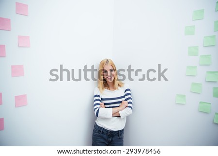Happy young woman with arms folded in casual cloth standing in a corner at office