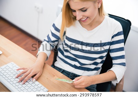 Happy young woman holding bank card and typing on keyboard in office