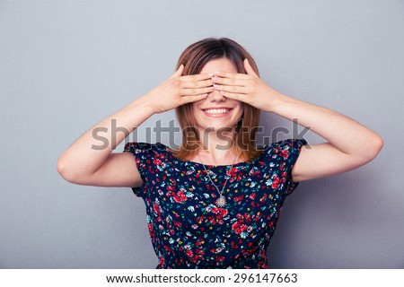 Happy young woman covering her eyes over gray background. Waiting for surprise