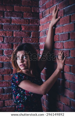 Scared young woman standing in corner of brick wall and looking away