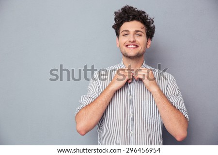 Happy young man buttoning shirt over gray background and looking at camera