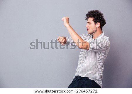 Young man listening music in headphones and dancing over gray background